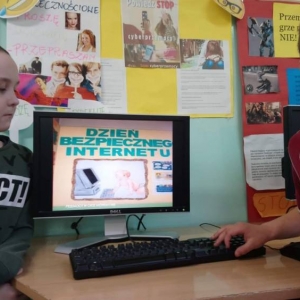 2 chłopców przed włączonym monitorem komputera z wykonanym przez siebie tematycznym plakatem.