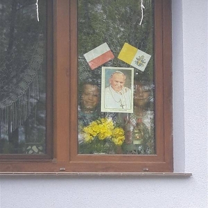 W oknie swojego domu, z powieszonym na szybie zdjęciem papieża i flagami Watykanu oraz ozdobionym żółtymi kwiatami w wazonie, uczennica i uczeń