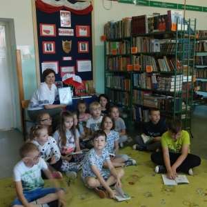 Nauczyciel biblioteki i grupa dzieci siedzą przed tablicą z gazetką tematyczną