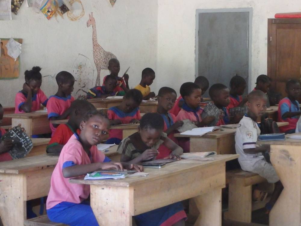Grupa dzieci z afrykańskiej szkoły siedzi w ławkach szkolnych ubrana w mundurki w różowo-niebieskich barwach