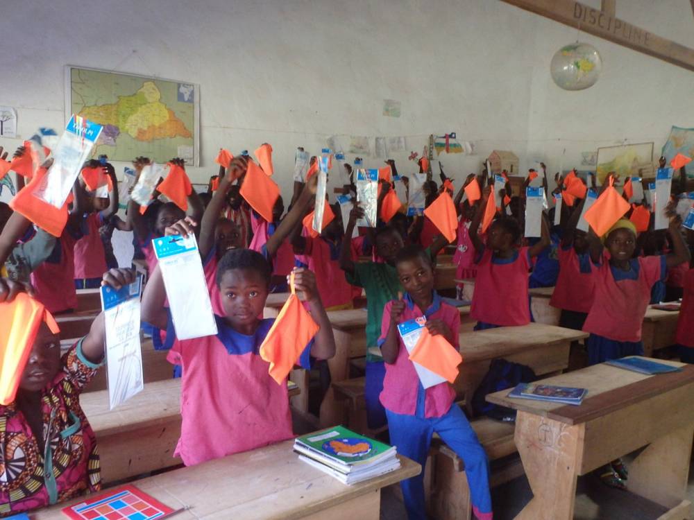 Grupa dzieci z afrykańskiej szkoły siedzi w łąwkach szkolnych ubrana w mundurki w różowo-niebieskich barwach