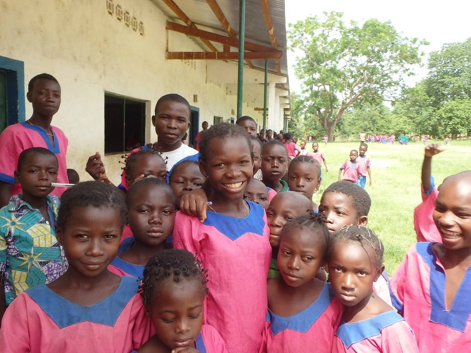 Grupa dzieci z afrykańskiej szkoły stoi na podwórku ubrana w mundurki w różowo-niebieskich barwach