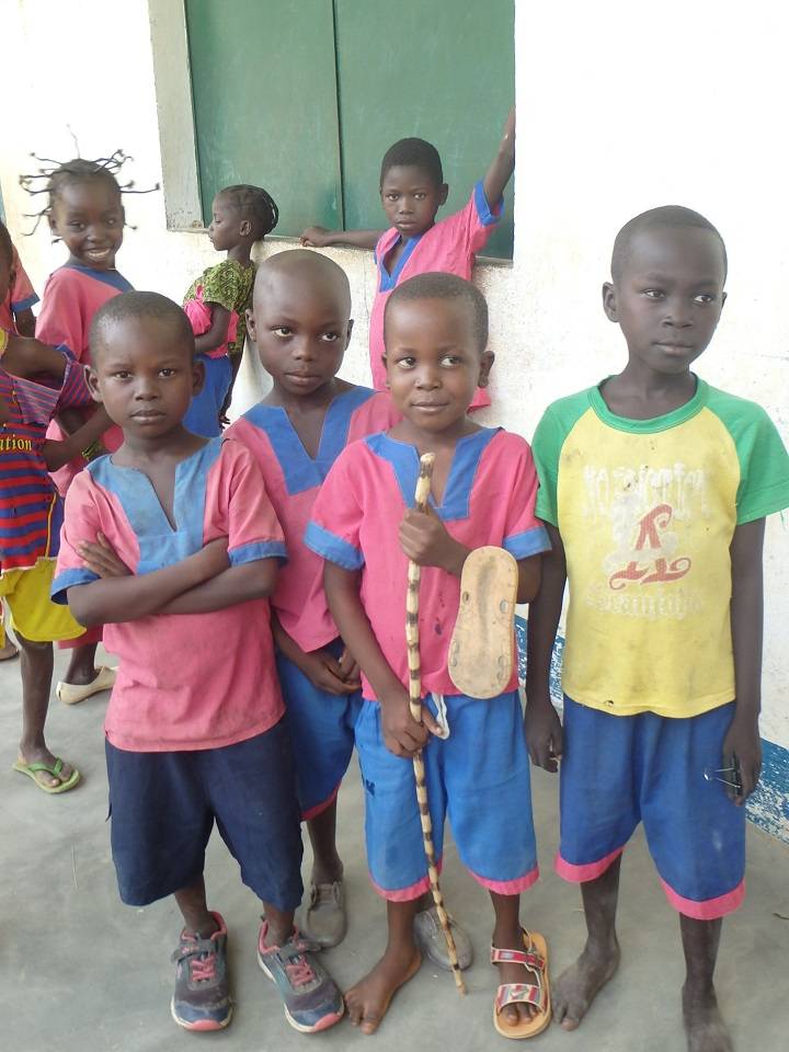 Grupa dzieci z afrykańskiej szkoły stoi przed budynkiem szkoły ubrana w mundurki w różowo-niebieskich barwach