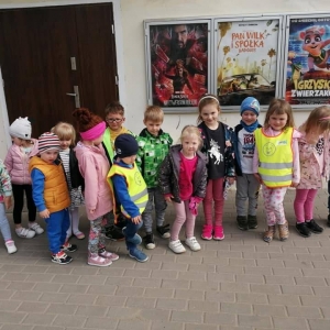 Fot. A. Waśk, Kino Grunwald w Olsztynku.  Na zdjęciu grupa dzieci 3 - 4  letnich stojących przed budynkiem kina w Olsztynku. W tle plakaty reklamujące repertuar kina.