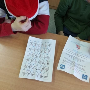 Uczniowie patrzą na kartkę z alfabetem w języku migowym
