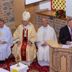 Arcybiskup i księża siedzą, przed nimi stoi przy ambonie przedstawiciel Rady Rodziców i czyta do mikrofonu
