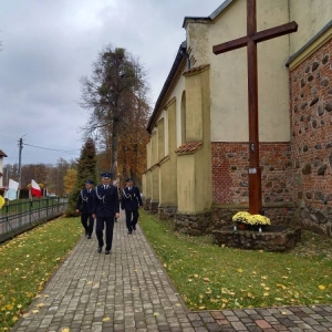 Trzech strażaków w mundurach idzie chodnikiem przy kościele