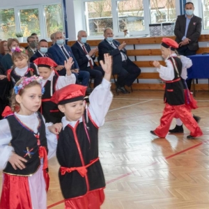 4 pary przedszkolaków tańczą krakowiaka, za nimi zebrani uczestnicy uroczystości przyglądają się