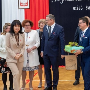 Dyrektor trzyma upominek, Przy nim stoi dyrekcja szkół gminnych i ZASiP w Olsztynku, uśmiechają się