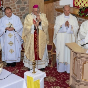 Arcybiskup, 3 księży i ministrant stoją, 1 ksiądz czyta do mikrofonu przy ambonie