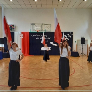 Taniec z flagami – uczennice idą w dwóch rzędach z flagami uniesionymi nad głowami