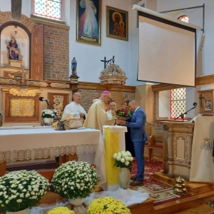 Przedstawiciele rodziców uczniów (kobieta i mężczyzna) wręczają Arcybiskupowi wiązankę kwiatów