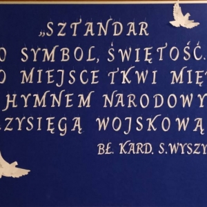 Na granatowej tablicy cytat BŁ. Kard. Wyszyńskiego „Sztandar to symbol, świętość. Jego miejsce tkwi między hymnem narodowym, a przysięgą wojskową.”