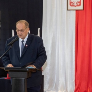 Burmistrz Olsztynka stoi przy mównicy na tle flagi Polski i  przemawia 