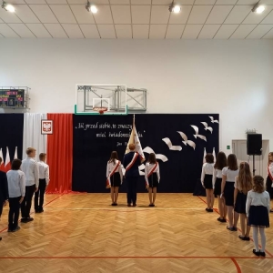 W centrum Poczet sztandarowy, a po obu ich stronach w dwóch rzędach przedstawiciele uczniów każdego oddziału stoją tyłem do zebranych i przodem do dekoracji