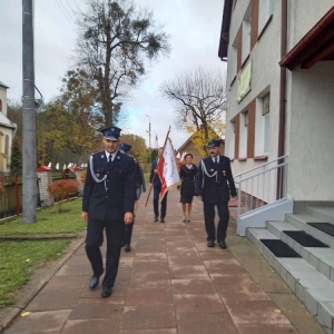 Chodnikiem przy budynku szkoły, w asyście OSP w Waplewie, przedstawiciele Rady Rodziców idą ze sztandarem