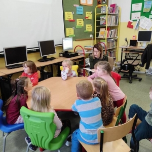 Na zdjęciu grupa dzieci siedzących przy stolikach w bibliotece.