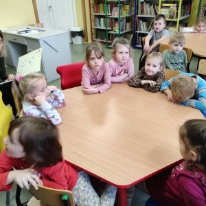 Na zdjęciu grupa dzieci siedzących przy stolikach w bibliotece.