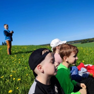 4 dzieci siedzi na trawie, obok stoi chłopiec z aparatem w rękach.