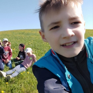 Selfie grupowe dzieci siedzących na trawie wykonane przez chłopca.