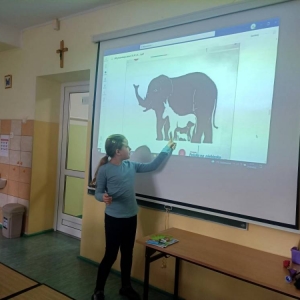 Uczennica oddziału II stoi przy wyświetlonej na projektorze prezentacji „Lekcja Autyzm” przygotowanej przez Fundację JiM – slajd z zadaniem „Jakie zwierzęta widzisz na obrazku?”. Palcem wskazuje na kontury osła.