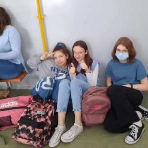 Podczas przerwy, na korytarzu szkolnym siedzą 4 uczennice oddziału VII a ubrane w niebieskie elementy garderoby. Trzy z nich siedzą na podłodze, jedna na ławeczce.