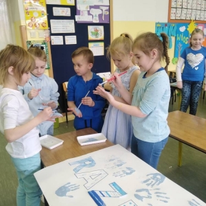 4 uczennice i uczeń oddziału I stoi przy ławce z plakatem i maluje niebieska farbą swoje dłonie.