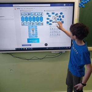 Czwartoklasista stoi i dłonią pokazuje na wyświetlone na monitorze infografiki na temat autyzmu.