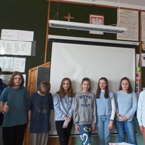 Siódmoklasiści (4 chłopców i 6 dziewczynek) pozuje do zdjęcia pamiątkowego. Wszyscy ubrani w niebieskie akcenty garderoby stoją w rzędzie w sali szkolnej.