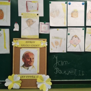 Rozwieszone na tablicy 12 rysunków wykonanych przez dzieci i zdjęcie - portrety Jana Pawła II, patrona szkoły.