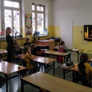 Wychowawczyni stoi, a uczniowie siedzą. Oglądają film realocjonujacy ostatnią wizytę Jana Pawła II w Polsce.
