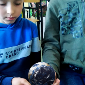 Dwaj chłopcy siedzą na podłodze, oglądają przestrzenny model Ziemi i poznają informacje o naszej planecie z wykorzystaniem smartfonu i interaktywnej karty edukacyjnej 4D.