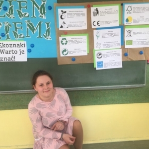 Siódmoklasistka, w świetlicy szkolnej, kuca pod tablicą, na której wywieszona jest wykonania przez nią tematyczna gazetka.