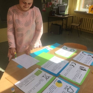 Siódmoklasistka w świetlicy szkolnej przygotowuje tematyczna gazetkę - porządkuje i układa na ławce zielone i niebieskie kartki A4, a na nich wydrukowane hasła i informacje o sposobach dbania o środowisko.