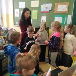 Grupa dzieci stoi wokół nauczycielki, która pokazuje im wydrukowany model 3d Polski.