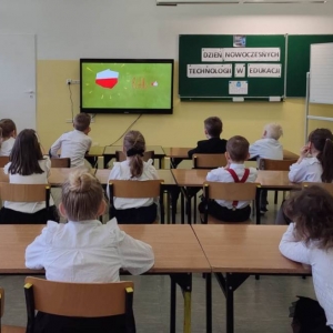 Uczniowie siedzą w ławkach, przed nimi wyświetlona bajka – animacja – slajd wskazujący, że Polska jest na bdb poziomie w zakresie wykorzystywania nowoczesnych technologii.