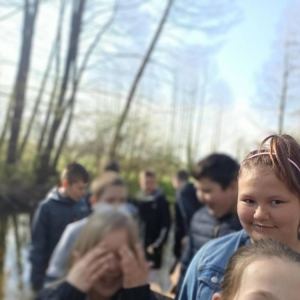 Liczna grupa czwartoklasistów podczas spaceru w okolicy szkoły w ramach zajęć przyrody. Na przedzie dziewczynka patrzy w kierunku osoby fotografującej.