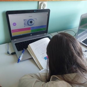 Uczennica, podczas zajęć j. angielskiego, siedzi przed laptopem, z otwartym zeszytem i rozwiązuje quiz online.