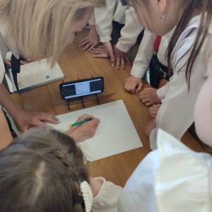 Wychowawczyni rysuje granice Polski z wykorzystaniem projektora i smartfonu. Dzieci zebrane wokół przyglądają się.