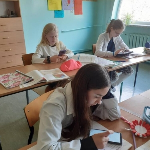 3 szóstoklasistki, podczas zajęć historii, siedzą przy ławkach. Na tabletach i smartfonach wykonują tematyczne ćwiczenia online.