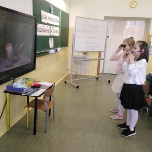 Dwie dziewczynki w okularach oglądają animowany film 3d, wyświetlony na telewizorze interaktywnym.