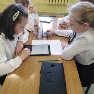 4 dziewczynki siedzą przy stoliku i z wykorzystaniem tabletu, wyszukują w internecie obrazków do rysowania z wykorzystaniem projektora.