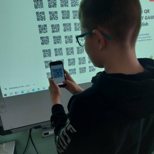 Uczeń, podczas zajęć j. angielskiego, przy pomocy smartfonu, wybiera i skanuje kod QR, spośród wyświetlonych na tablicy interaktywnej.