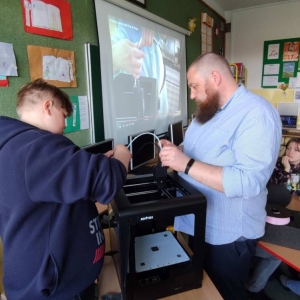 Nauczyciel i ósmoklasista podłączają drukarkę 3d zgodnie z instrukcją wyświetlaną na projektorze.