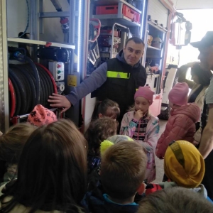 Przedstawiciel OSP pokazuje i opisuje dzieciom nawinięty wąż znajdujący się w wozie strażackim.