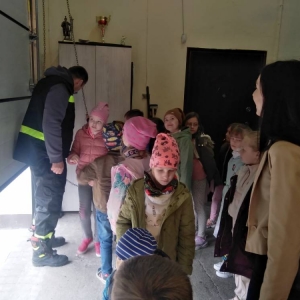 Grupa uczniów, nauczycielka i przedstawiciel OSP podczas zamykania wjazdu do remizy.