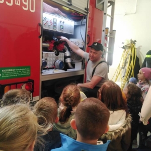 Przedstawiciel OSP pokazuje i opisuje dzieciom sprzęty znajdujące się w wozie strażackim.