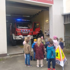 Przedstawiciel OSP włączył światła wozu strażackiego. Dzieci stoją naprzeciwko i się przyglądają.