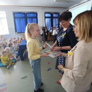 Dziewczynka  ubrana w żółtą bluzeczkę i niebieskie spodnie odbiera nagrodę w konkursie.   